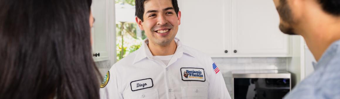 Benjamin Franklin Plumbing technician Diego talking to a couple in a kitchen.