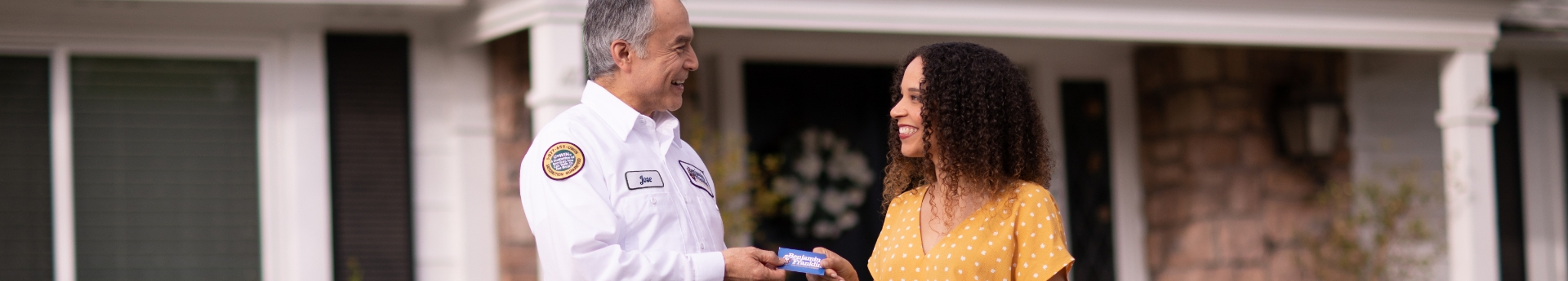 Benjamin Franklin Plumbing technician handing a card to a smiling woman in front of a house.